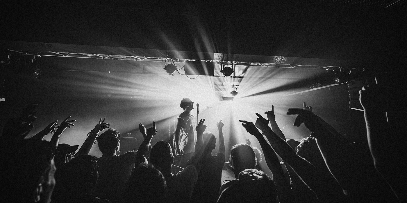 Modestep steht auf einer Bühne im Scheinwerferlicht und singt, während man die Hände aus dem Publikum sieht.