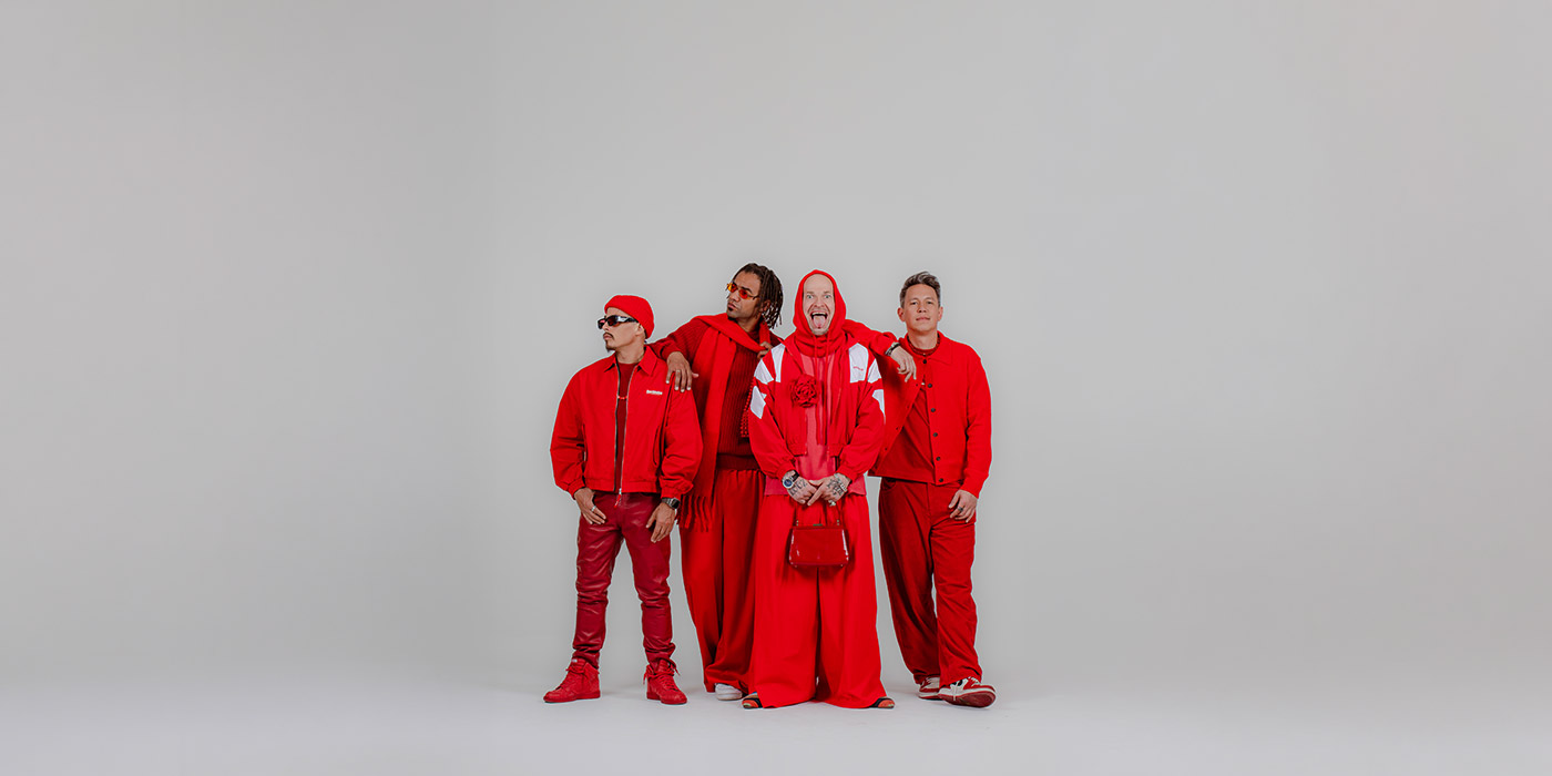 Die 4 von Culcha Candela sind rot gekleidet und stehen vor einem weiß/beigen Hintergrund. Sie sind mit ihrem ganzen Körper zu sehen und posen für die Kamera.