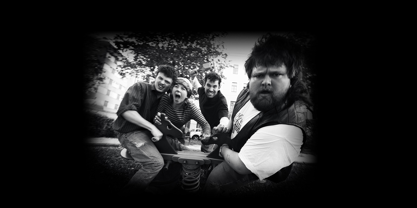 Schwarzweiß Foto von den 4 Bandmitgliedern wie sie alle auf einer Wippe am Spielplatz sitzen und mit viel Energie und verschiedenen Grimassen Richtung Kamera lehnen