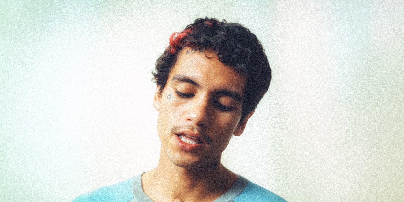 Dominic Fike is displayed in portrait, gaze downwards, mouth slightly open as if singing or talking.